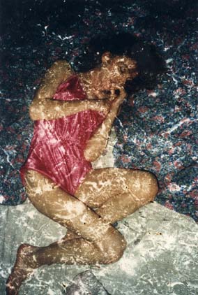 Femme brune en body de satin rose allongée sur des coussins.