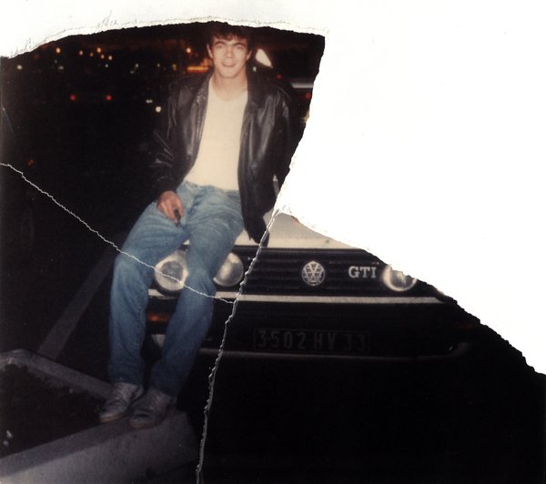 Jeune homme assis sur le capot d'une voiture de nuit, ville en arrière-plan. Image avec déchirure, reconstituée.ᴬᴵ