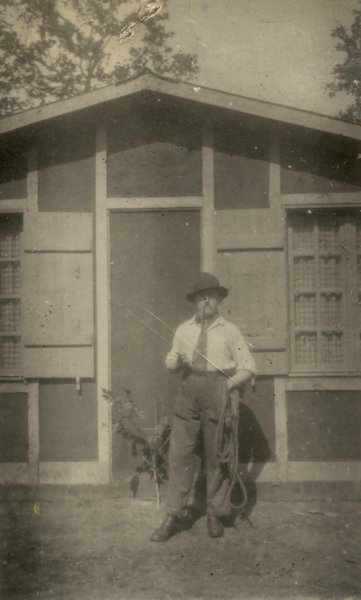 Homme à chapeau debout devant une façade. Noir et blanc.