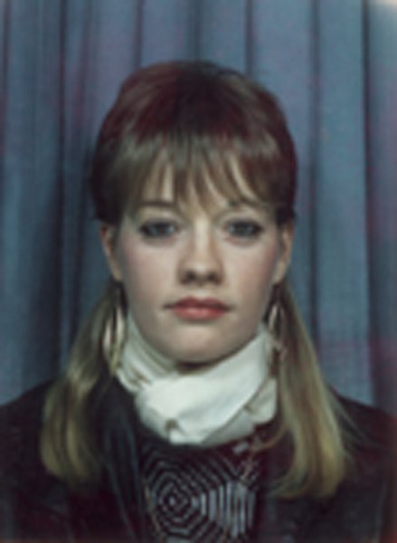 Visage de jeune femme blonde, avec des anneaux aux oreilles et écharpe blanche.
