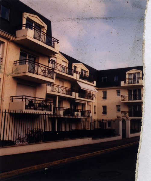 Façade d’immeuble avec balcons et jardinets séparés par une grille.