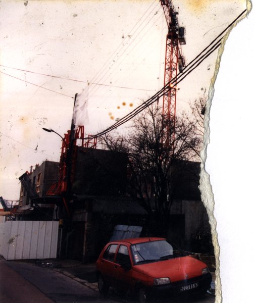 Voiture rouge garée, grue en arrière-plan.