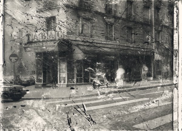 Coin de rue avec bar tabac et passage piéton. Image abîmée. Noir et blanc.