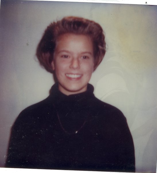 Buste de femme blonde souriante avec pull sombre.