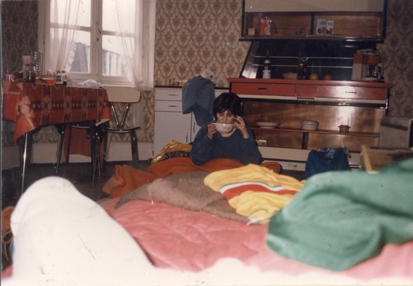 Femme assise un bol à la main au milieu de sacs de couchage dans une cuisine.