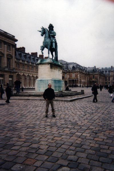 Homme devant la statue de Louis XIV dans la cour pavée du château de Versailles.