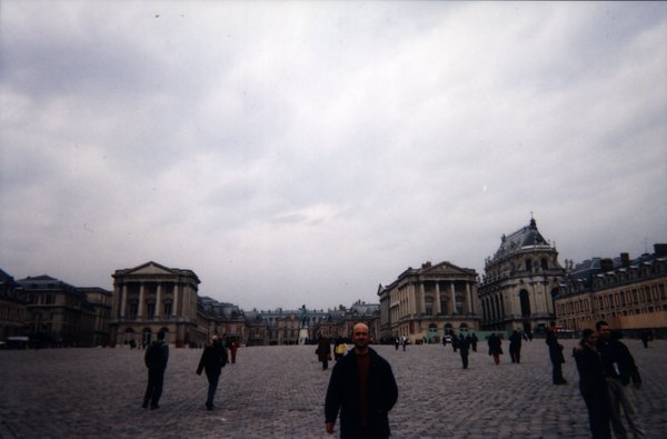 Homme devant la cour  pavée du château de Versailles.