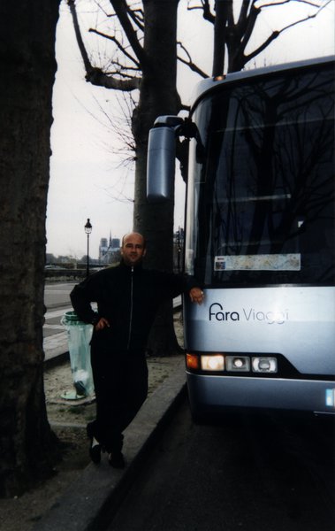 Homme debout le coude posé  sur le capot d’un autocar touristique.