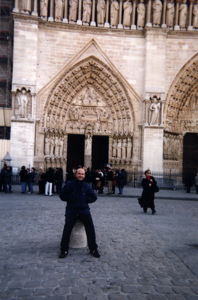 Homme assis sur un plot en pierre devant le tympan de la cathédrale Notre-Dame de Paris.