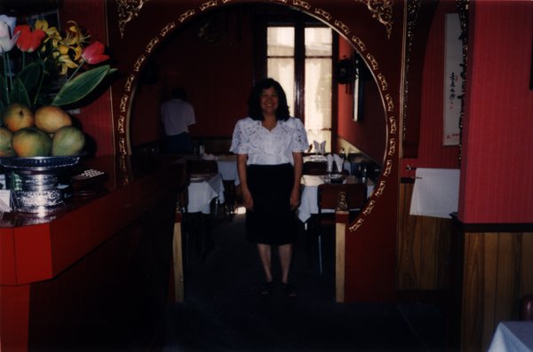 Femme debout souriante au milieu d’une salle de restaurant.