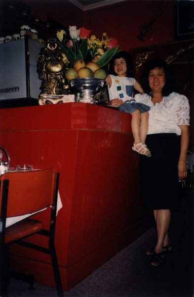 Femme accoudée à un comptoir et petite fille riant assise sur un comptoir.