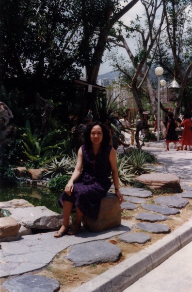 Femme assise sur un rocher artificiel dans l’allée d’un parc.