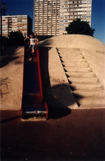 Petite fille en haut d’un toboggan, immeubles en arrière-plan.