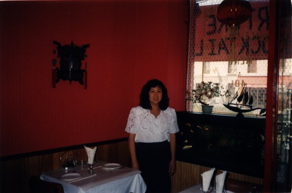 Femme brune debout devant des tables dans un restaurant.