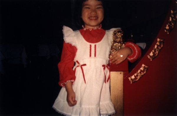 Petite fille souriante debout en robe rouge et blanche.