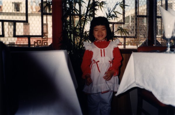 Petite fille souriante debout en robe rouge et blanche.