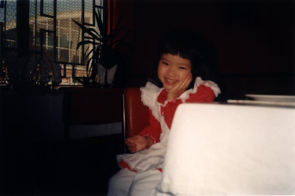 Petite fille souriante assise une main sur la joue.