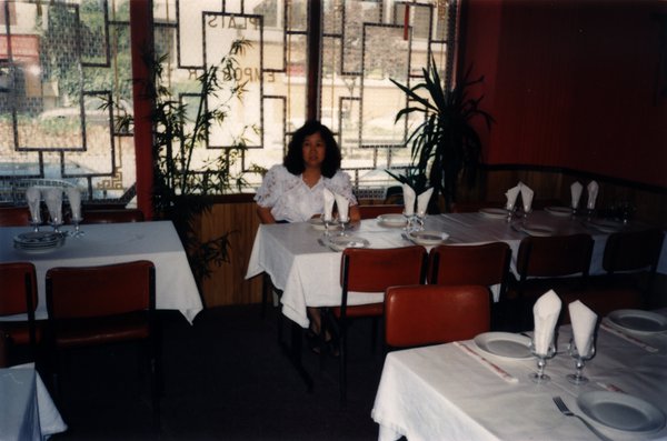 Femme brune en chemisier blanc assise à une table de restaurant.