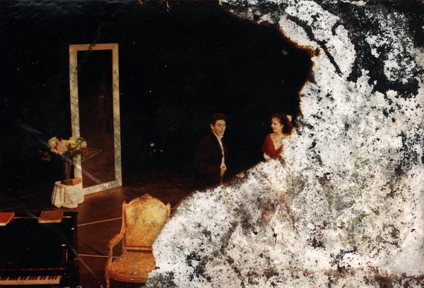 Homme en noir et femme en rouge et piano droit. Image abîmée.