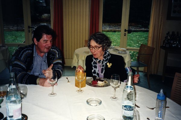 Femme à lunettes souriante assise à une table, souffle sur une bougie.