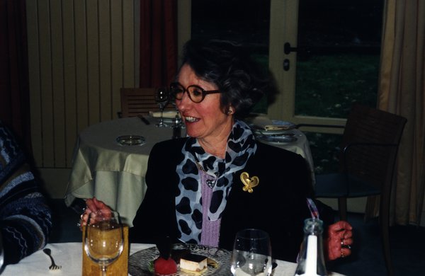 Femme à lunettes souriante assise à une table devant des pâtisseries.