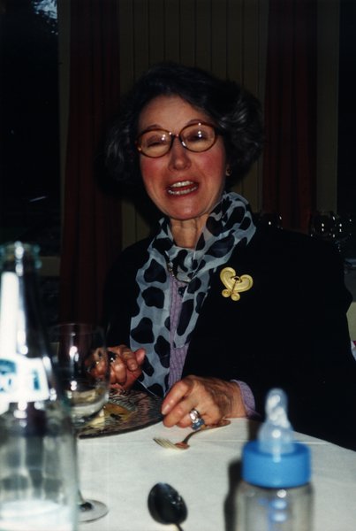 Femme à lunettes souriante assise à une table devant des pâtisseries.
