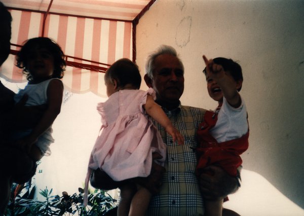 Homme âgé souriant avec deux enfants dans les bras.