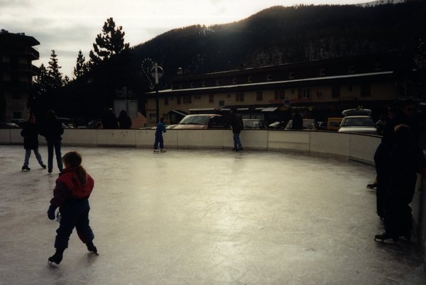 Patinoire avec enfants et adultes sur des patins, montagnes en arrière-plan.