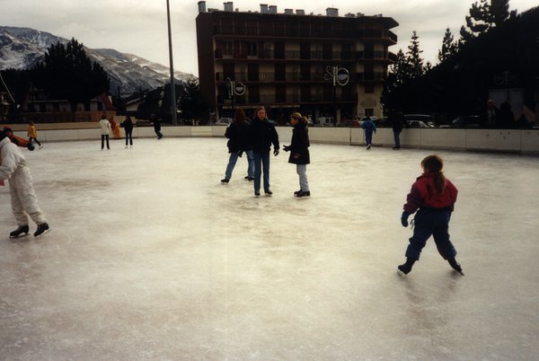 Patinoire avec enfants et adultes sur des patins, montagne en arrière-plan.