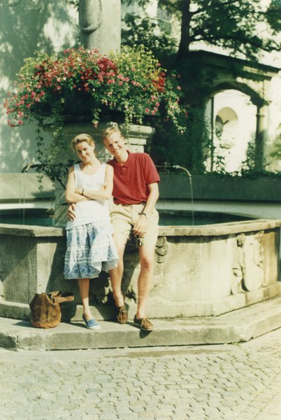 Couple d’homme et femme blond  posent enlacé au bord d’une fontaine.
