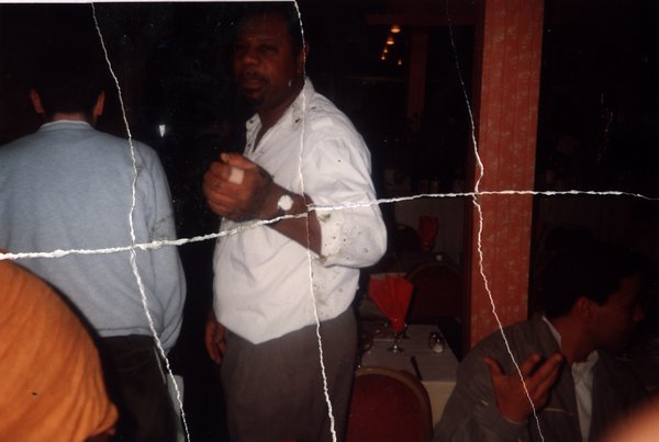 Homme debout dans un restaurant avec des convives attablés. Image avec déchirure, reconstituée.ᴬᴵ