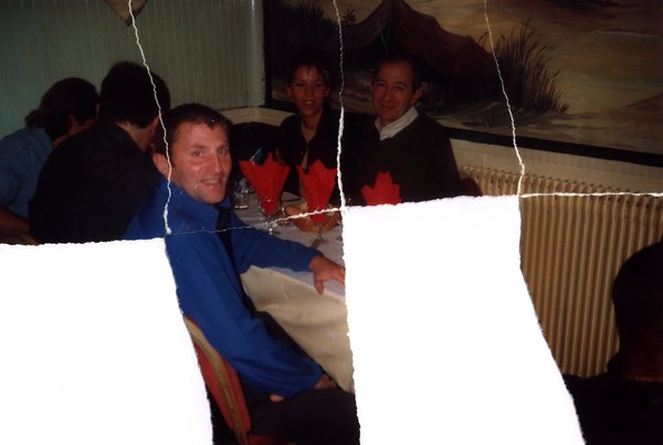 Repas de groupe avec homme en chemise bleue tourné vers l'objectif. Image avec déchirure, reconstituée.ᴬᴵ
