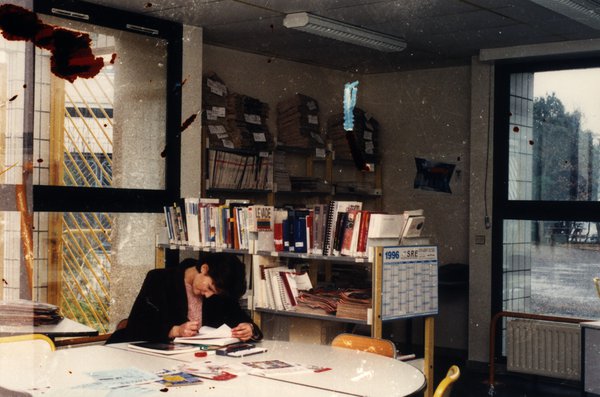 Personne penchée sur des papiers dans une salle avec étagères de classeurs. Image abîmée.ᴬᴵ
