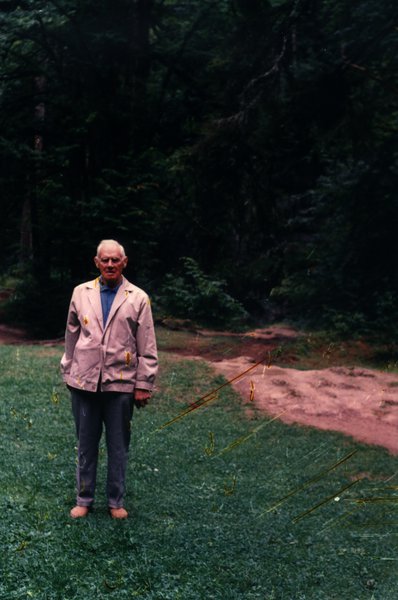 Homme âgé debout pieds nus sur l'herbe près d'un chemin forestier.ᴬᴵ