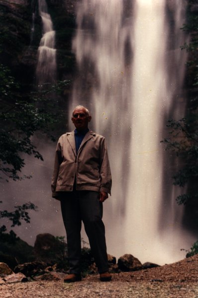 Homme âgé debout devant une cascade.ᴬᴵ