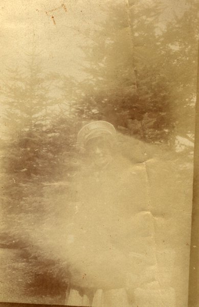 Silhouette floue d'une personne avec un chapeau devant des sapins. Photo très délavée. Noir et blanc.ᴬᴵ