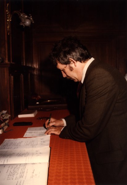 Homme signant des documents à un bureau en bois.ᴬᴵ