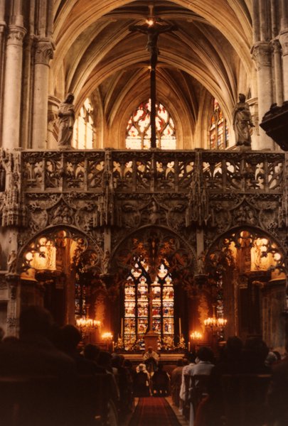 Intérieur d'une église gothique avec jubé sculpté et vitraux, cierges allumés.ᴬᴵ