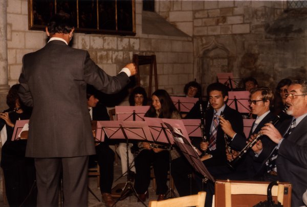 Chef d'orchestre dirigeant un ensemble de musiciens dans une église en pierre.ᴬᴵ