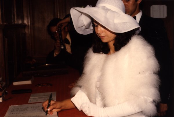 Femme en chapeau blanc et étole en fourrure signant un registre.ᴬᴵ