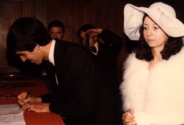 Marié signant le registre, mariée en chapeau blanc à ses côtés.ᴬᴵ