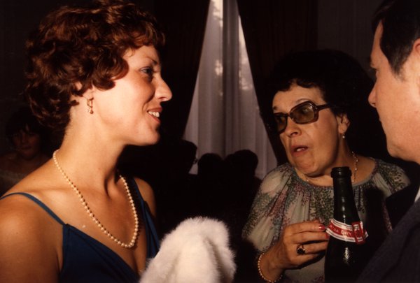 Femme aux cheveux bouclés discutant avec une femme à lunettes de soleil et un homme.ᴬᴵ