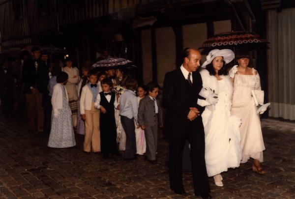Cortège de mariage sous la pluie, invités avec parapluies devant un bâtiment à colombages.ᴬᴵ