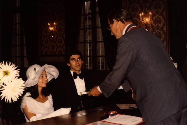 Cérémonie de mariage civil, mariés assis à une table face à un officiel.ᴬᴵ