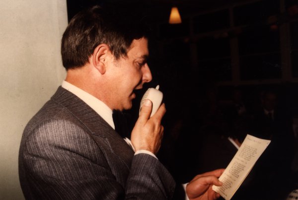 Homme en costume gris parlant au micro en lisant un papier.ᴬᴵ