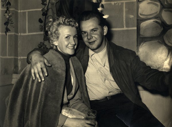 Jeune homme et jeune femme enlacés devant une porte en pierre. Noir et blanc.ᴬᴵ