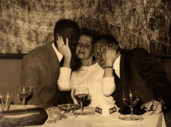 Trois personnes plaisantant à une table, verres de vin. Noir et blanc.ᴬᴵ