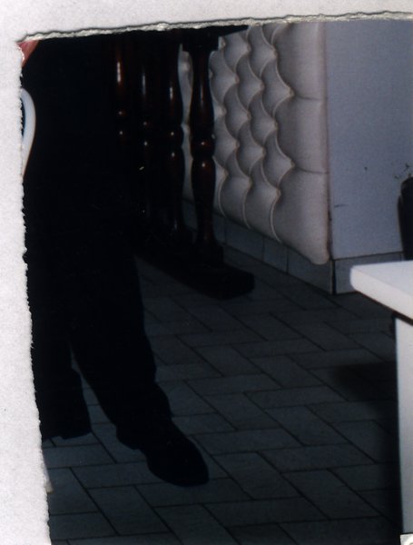 Pieds et jambes près d'une banquette, image sombre. Fragment déchiré.ᴬᴵ