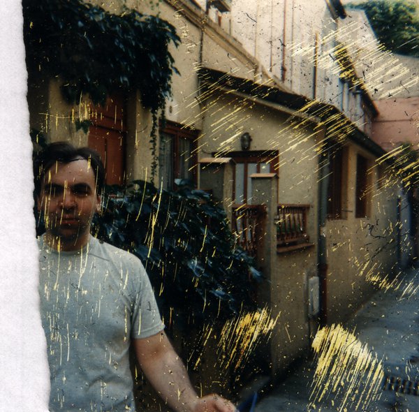 Homme debout devant une maison couverte de plantes grimpantes, ruelle. Photo rayée.ᴬᴵ