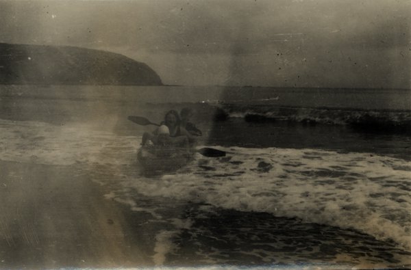 Deux personnes dans un canoë dans les vagues près du rivage. Image très pâlie. Noir et blanc.ᴬᴵ